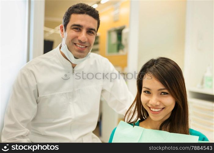 photo of smiling caucasian dentist sitting next to his female patient and looking towards the camera