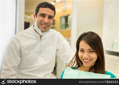 photo of smiling caucasian dentist sitting next to his female patient and looking towards the camera