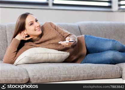 photo of smiling caucasian woman lying on the couch and looking tv