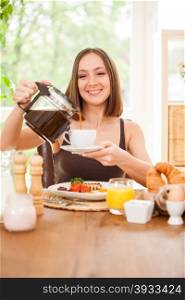 Photo of smiling caucasian woman pouring a cap of coffee while having breakfast at home