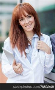 photo of smiling female doctor standing outside with tablet pc