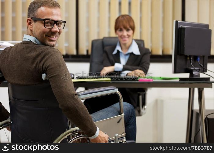 photo of smiling man on wheelchair looking towards the camera while female manager is sitting on a chair in the background