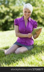Photo of smiling woman with tablet pc is sitting on the grass while smiling