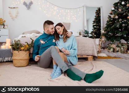 Photo of stylish loving man and pregnant woman with sparklers on background of Christmas decorations.. Photo of stylish loving man and pregnant woman with sparklers on background of Christmas decorations