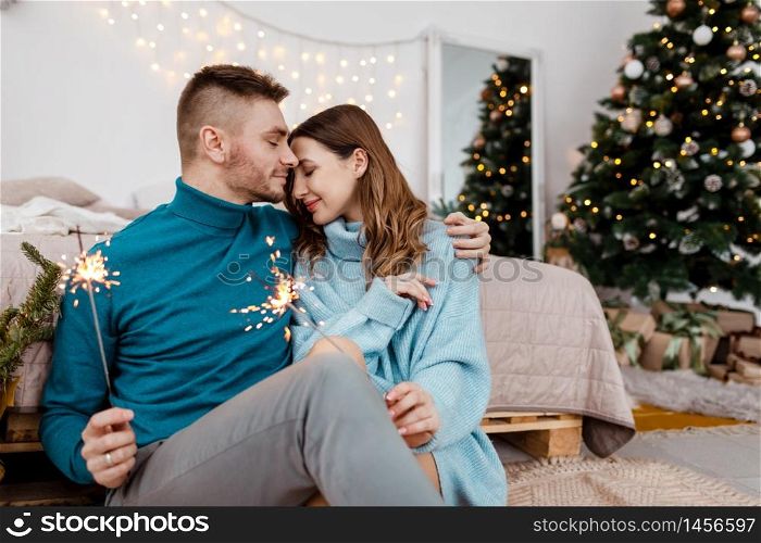 Photo of stylish loving man and pregnant woman with sparklers on background of Christmas decorations.. Photo of stylish loving man and pregnant woman with sparklers on background of Christmas decorations