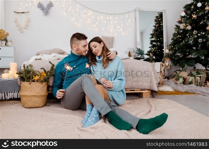 Photo of stylish loving man and pregnant woman with sparklers on background of Christmas decorations.. Photo of stylish loving man and pregnant woman with sparklers on background of Christmas decorations