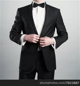 Photo of stylish man in elegant black suit with tie. Fashionable young model pose in photography studio. Luxury evening smoking with white shirt.