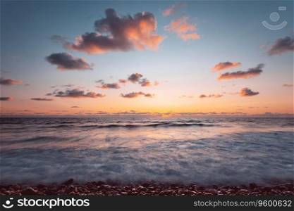 Photo of the azure seashore, gently covered by the velvet sunset . Small beach waves, as if playing and teasing the shore, then advance and retreat. Peaceful landscape.. Beautiful sea landscape in sunset light
