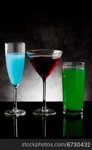 photo of three cocktails on black glass counter with grey lighted background