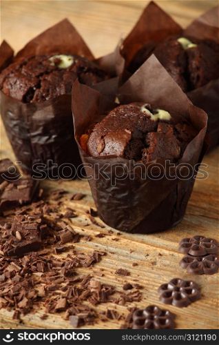 Photo of three moist chocolate muffins resting on an old wood table. Shallow depth of field focusing on front muffin.