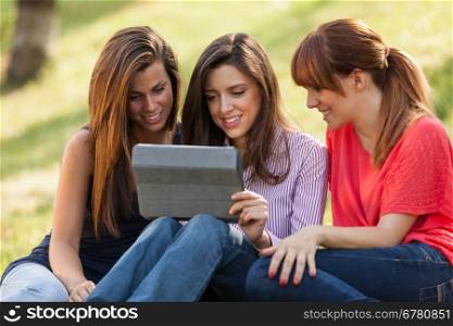Photo of threee woman sitting on grass while looking at a digital screen