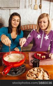 Photo of two beautiful women dipping bread into the melted cheese in a fondue pot.