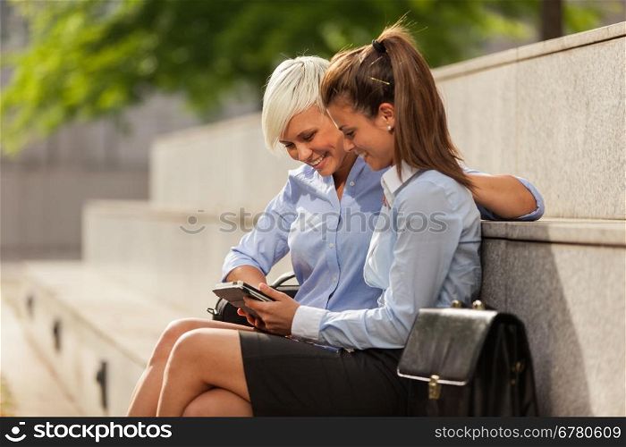 Photo of two businesswoman sitting outside while looking at a tablet