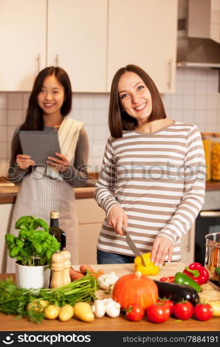Photo of two smiling female friends cooking together at home