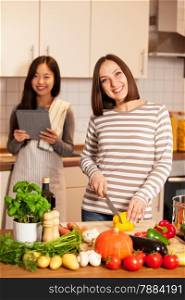 Photo of two smiling female friends cooking together at home