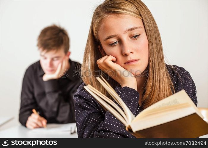 Photo of two teenagers in a classroom reading and studying.