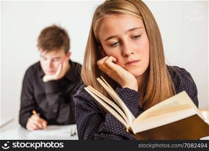 Photo of two teenagers in a classroom reading and studying.
