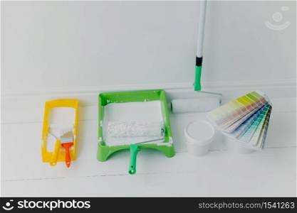 Photo of two trays with paint rollers, bucket with color and colour samples, white background. House renovation concept. Refurbishment