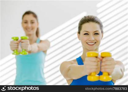 Photo of two young smiling women are doing exercises with dumbbells in gym