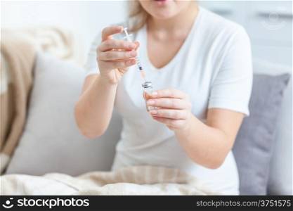 Photo of woman lying in bed and filling syringe with medicines