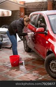 Photo of woman washing red car with rug outdoors
