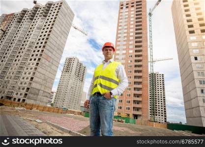 Photo of young engineer in hardhat against construction site