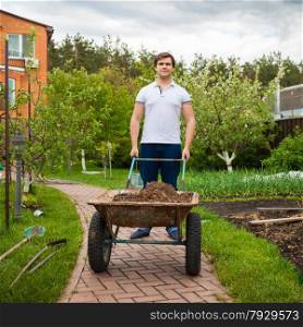 Photo of young man carrying garden wheelbarrow