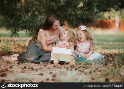 Photo of young mother with two cute kids reading book outdoors in spring time, happy mom teaching her children in the park, happy family, mom and two daughters. Mother&rsquo;s day concept.. Photo of young mother with two cute kids reading book outdoors in spring time, happy mom teaching her children in the park, happy family, mom and two daughters. Mother&rsquo;s day concept