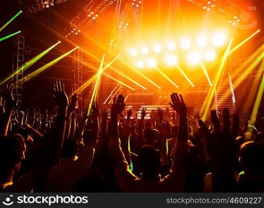 Photo of young people having fun at rock concert, active lifestyle, fans applauding to famous music band, nightlife, dj on the stage in the club, crowd dancing on dancefloor, night perfomance