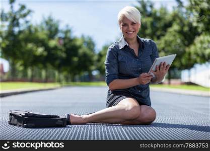 photo of young smiling business woman sitting on a metal floor with tablet pc