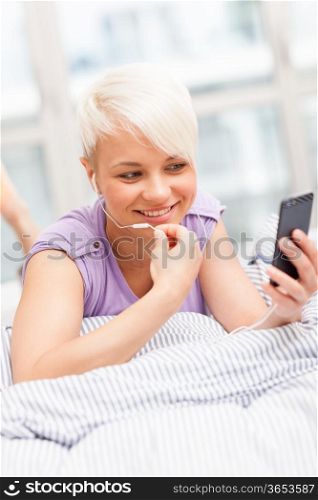 Photo of young woman phoning in the bed with headphones