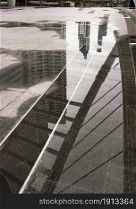 "Photo reflections of bridge structure, buildings and sky above a puddle of rain water on the skywalk to skytrain station at "Chong Nonsi" Copy space, No focus, specifically."