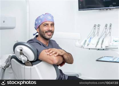 Photo with copy space of a male dentist siting on a chair into a clinic room with medical equipment. Photo with copy space of a dentist siting on a chair into a clinic room