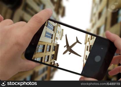 photograph a flying plane over the city on a smartphone. photograph a flying plane