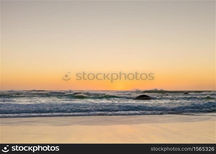 Photographed on a West coast facing beach in Cape Town South Africa. Rough waves at sunset on a sandy beach with reflections on the water