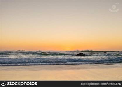 Photographed on a West coast facing beach in Cape Town South Africa. Rough waves at sunset on a sandy beach with reflections on the water
