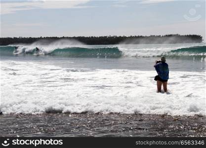 Photographer and serfers on wave near Pantai Sorake beach, Indonesia