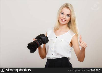 Photographer girl shooting images. Attractive blonde happy woman taking photos with camera making thumb up hand gesture, on gray