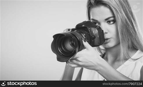 Photographer girl shooting images. Attractive blonde woman taking photo with camera. Black white photo