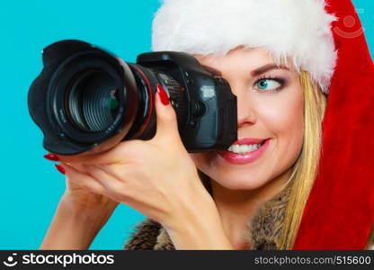 Photographer girl shooting images. Attractive blonde woman wearing santa claus helper hat taking photos with camera. Vivid blue background