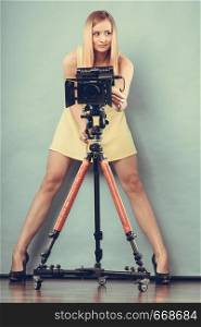 Photographer girl shooting images. Attractive fashionable blonde woman in full length taking photos with camera on blue