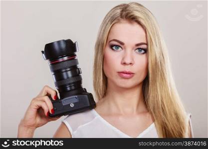 Photographer girl shooting images. Lovely blonde woman with professional camera on gray background