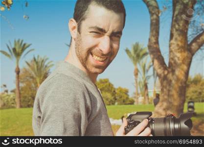 Photographer holding a digital camera and smiling to camera.