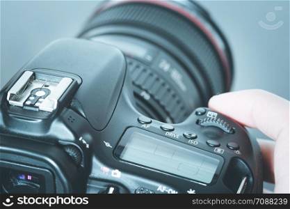 Photographer is holding a professional camera with telephoto lens in his hand, laptop in the blurry background