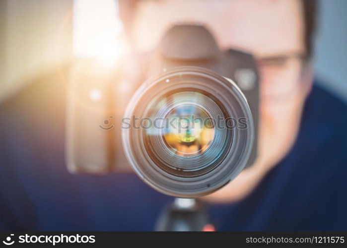 Photographer is standing behind a professional camera with telephoto lens on a tripod. Sunbeam.