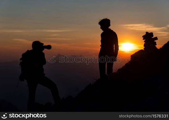 Photographer performs photography to a girl at sunset in high mountains in silhouettes.