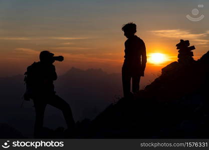 Photographer performs photography to a girl at sunset in high mountains in silhouettes.