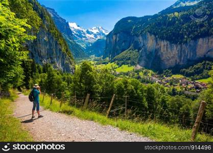 Photographer traveler takes a photo on mountain walking trail from Wengen to village of Lauterbrunnen with the Staubbach Fall, and the Lauterbrunnen Wall in Swiss Alps, Switzerland.. Mountain village Lauterbrunnen, Switzerland
