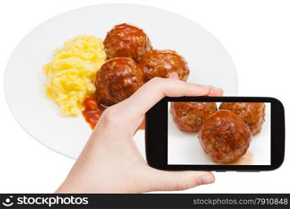 photographing food concept - tourist takes picture of roasted meatballs under meat sauce and mashed potato on plate on smartphone, Sweden