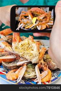 photographing food concept - tourist takes picture of seafood plate with crab, prawns, shrimps on smartphone, France